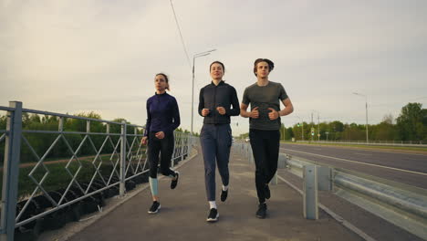 Jóvenes-Amigos-Corren-Juntos-Por-La-Mañana-A-Lo-Largo-De-La-Carretera-En-La-Ciudad-Manteniendo-Un-Estilo-De-Vida-Saludable-Y-En-Forma